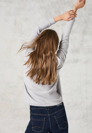 Grau gestrickter Pullover mit Rundhalsausschnitt, kombiniert mit dunkelblauen Jeans aus Denim, die über Gesäßtaschen und kontrastierende Nähte verfügen.