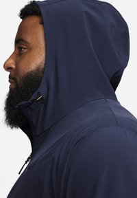 Mörkblå hoodie med hög krage och justerbar huva, med en slät yttre textur och dragkedja framtill.