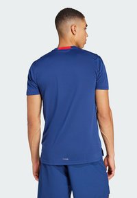 Marinblå atletisk t-shirt med röd accent vid nacke bak, tillverkad av lättviktsmaterial, med korta ärmar och rund halsringning.