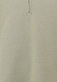 Lys beige kvart-zip genser, strikket tekstur, med metallglidelås og sydd detaljer langs åpningen.