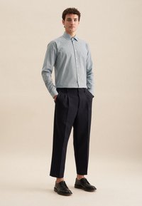 Camicia a righe blu chiaro e bianca con colletto, abbinata a pantaloni alti blu scuro. Scarpe in pelle nera completano l'outfit.