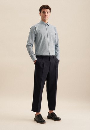 Hellblau-weiß gestreiftes Hemd mit Kragen, kombiniert mit hoch geschnittenen marineblauen Hosen. Schwarze Lederschuhe vervollständigen das Outfit.