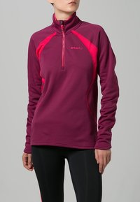 Långärmad, zip-up fleece-tröja i mörklila med klara rosa detaljer och hög krage. Har en smal passform och mjuk textur.