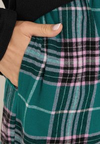 Teal ruudullinen vaate, jossa on mustia, valkoisia ja vaaleanpunaisia yksityiskohtia; sisältää taskun ja pehmeän tekstuurin; seuranaan musta ribbikuvioinen paita.