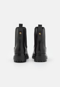 Botas de cuero negro hasta el tobillo con paneles laterales elásticos, talón reforzado y suelas de goma gruesa. Presenta un acento del logo dorado en la parte trasera.