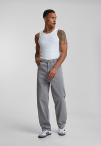 Gray loose-fit trousers made of denim, paired with a white tank top. The outfit is complemented by black and white sneakers.