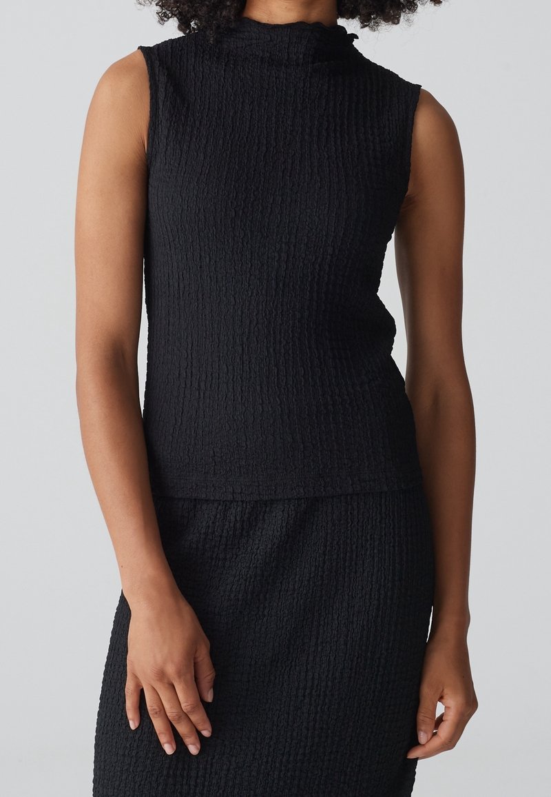 Haut sans manches noir avec un col montant, fabriqué en tissu texturé. Présente une silhouette ajustée et des nervures subtiles sur l'ensemble du matériau.