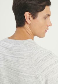 Suéter de punto gris claro con sutiles rayas horizontales, cuello redondo acanalado y textura suave. Enfoque en el área de los hombros y el cuello.