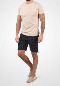 T-shirt beige clair texturé à manches courtes associé à un short noir avec cordons de serrage. Tenue complétée par des chaussures beige à enfiler.