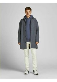 Gray wool coat with a hood, button closure, and side pockets, layered over a blue hoodie. Model wears white jeans and sporty shoes.