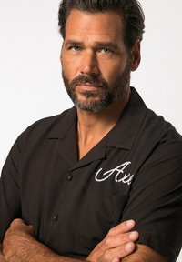 Czarna koszula krótko rękawowa z zapięciem na guziki, z kieszonką i białymi haftowanymi detalami, nadająca gładki i wyraźny wygląd.