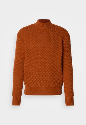 Räsyinen oranssi neulepaita, jossa on korkea kaulus, röyhelötyynyt ja helma, sekä paksu, kuvioitu muotoilu.