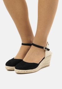Les wedges espadrilles en suède noir ont une semelle en corde de jute, une bride à la cheville avec une boucle et un accent arrière en tissu texturé.