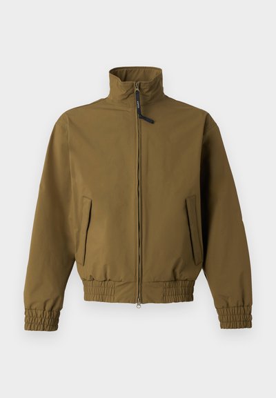 Veste marron à fermeture éclair avec col montant, poignets et taille élastiques, comprenant deux poches avant et un curseur de fermeture éclair noir.