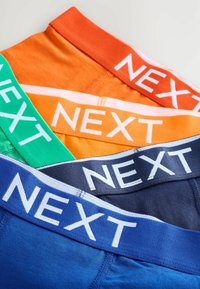 Quatre paires de sous-vêtements pour hommes avec des ceintures élastiques contrastées en orange, vert, marine et bleu, toutes avec "NEXT" en lettres blanches.
