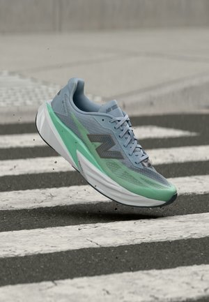 Chaussure de course New Balance bleu clair et verte flottant au-dessus d'un passage piéton noir et blanc dans une rue.