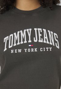 Camiseta negra de algodón con escote redondo. Presenta un texto en blanco en negrita: "TOMMY JEANS NEW YORK CITY" y un pequeño detalle de logo en rojo y azul.