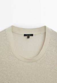 Pull en maille beige à col rond avec une texture douce et une étiquette noire cousue à l'intérieur du col arrière.