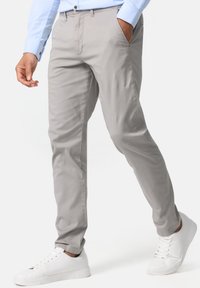 Pantalons gris clair à coupe ajustée, avec poches latérales et texture subtile, accompagnés de baskets blanches et d'une chemise bleue à boutons.