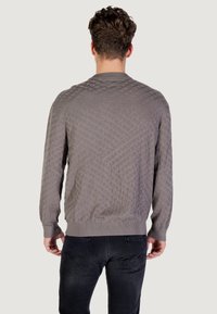 Pull en tricot matelassé gris avec une texture à motifs, des poignets et un ourlet côtelés. Stylisé avec un jean sombre, vu de l'arrière.