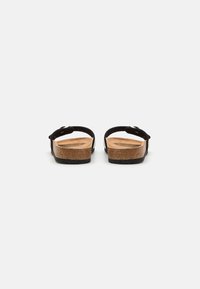 Sorte lærsandaler med justerbare remmer, korksåle og teksturert svart gummisåle. Vist fra baksiden, som viser et minimalistisk design.