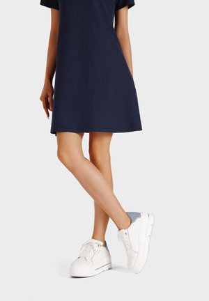 Sneakers bianchi con suola spessa e dettagli in camoscio grigio, abbinate a un vestito blu navy. Presentano punta rotonda e lacci frontali.