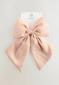 Un nœud en tissu rose avec une texture lisse, présentant un nœud central et de longues queues flottantes, fixé à un support en carton.