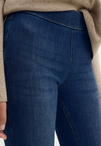 Los jeans de denim azul oscuro cuentan con una textura suave y una silueta ajustada, acentuada por costuras claras cerca de la cinturilla y las caderas.