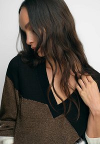 Struktuurne sviiter sügava V-kaelusega, millel on musta, kuldse ja valgega värvi plokkide disain. Näitab kudumiskangast erinevate mustritega.