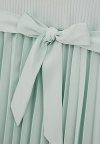 Mentolové šaty s plisovanou sukní a měkkým látkovým páskem svázaným do mašle v pase, s žebrovanou horní částí.