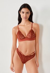 Kanten bralette en bijpassende string in diep rood, met driehoekige cups, decoratieve ringen en ingewikkelde kanten patronen met gladde randen.