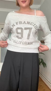 Felpa grigia a maniche lunghe con design a spalle scoperte, che presenta la scritta "San Francisco 97 California" in caratteri scuri. Indossata con pantaloni neri.