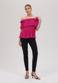 Fuchsia off-shoulder topp med volanger, plisséstruktur, sammen med svarte skinny jeans og svarte høyhælede sandaler.