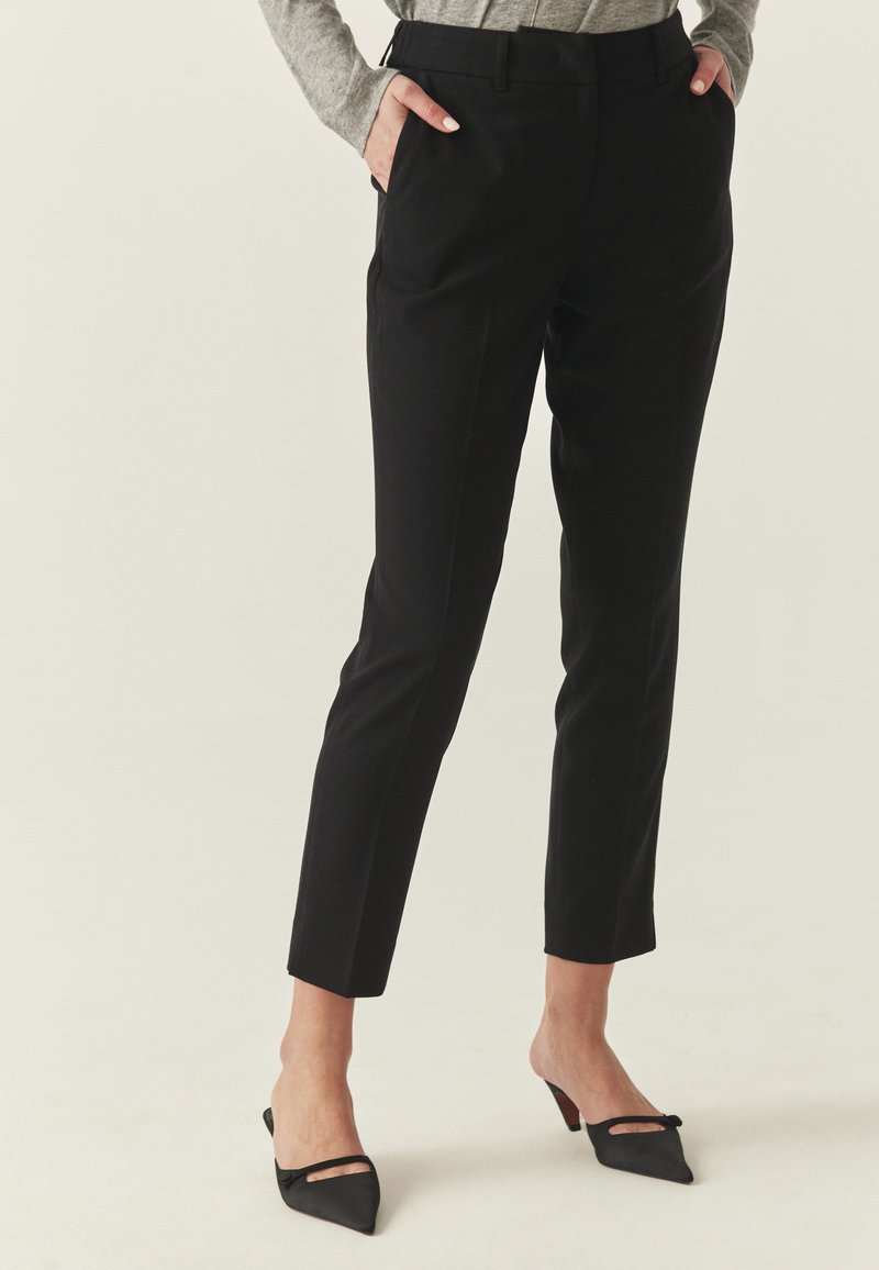 Pantalons noirs sur mesure avec une coupe ajustée, dotés de poches latérales et d'un tissu lisse. Le design comprend des ourlets retroussés et une taille mi-haute.