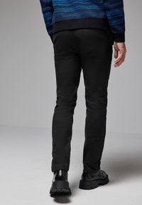 Svarta slim-fit-byxor i mjukt tyg, med slät yta och minimal detaljer, tillsammans med svarta skor med tjock sula.