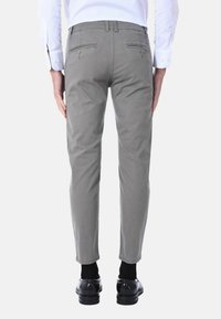 Chinos grigi con una vestibilità slim, dotati di tasche posteriori con chiusura a bottone. Indossati con una camicia bianca e scarpe nere, che mostrano un design pulito.