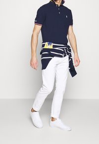 Námořnické polokošile s límečkem, bílými doplňky a vyšitým logem; bílé úzké kalhoty; svetr se zavázanými proužky; bílé tenisky.