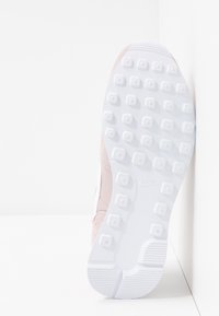 Semelle d'une basket Nike blanche avec des crampons carrés surélevés et un talon texturé, vue du dessous sur un fond blanc.