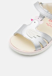 Silver läder sandaler för småbarn med ett hönsdesign. Har rosa detaljer, öppen tå-stil, och en texturerad, vit gummisula.
