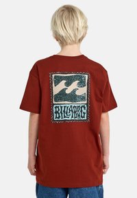 Camiseta de algodón color granate con un gran gráfico en la parte posterior que presenta un diseño de olas en tonos verde azulado y crema, delimitado por un contorno negro texturizado. Manga corta.