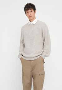 Light gray, knitted sweater with ribbed texture and round neckline, paired with beige cargo pants featuring side pockets.