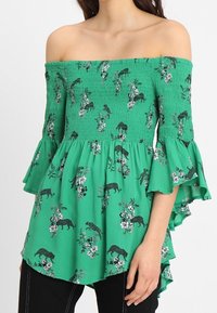 Top verde senza spalline con busto arricciato, maniche a volant, fantasie floreali e maculate, e un design a emiliano alto-basso.