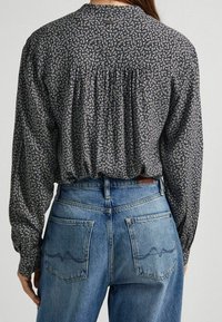 Blusa negra de flores con mangas largas, con detalles fruncidos en la parte posterior, combinada con jeans de mezclilla azul de cintura alta que tienen bolsillos traseros y acentos de costura.