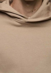 Felpa con cappuccio beige indossata da una persona, che mostra il collo e parte della zona del petto.