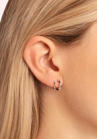 Orecchini a cerchio in argento, uno grande e uno piccolo, con una finitura lucida. Design semplice, posizionati in un orecchio forato, che mettono in risalto le texture lisce.