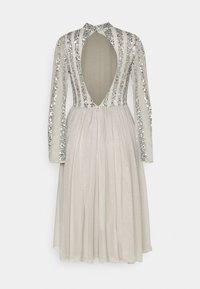 Robe embellie de sequins en beige clair avec des manches longues, un dos nu et une jupe plissée. Présente un col haut et un éclat subtil.