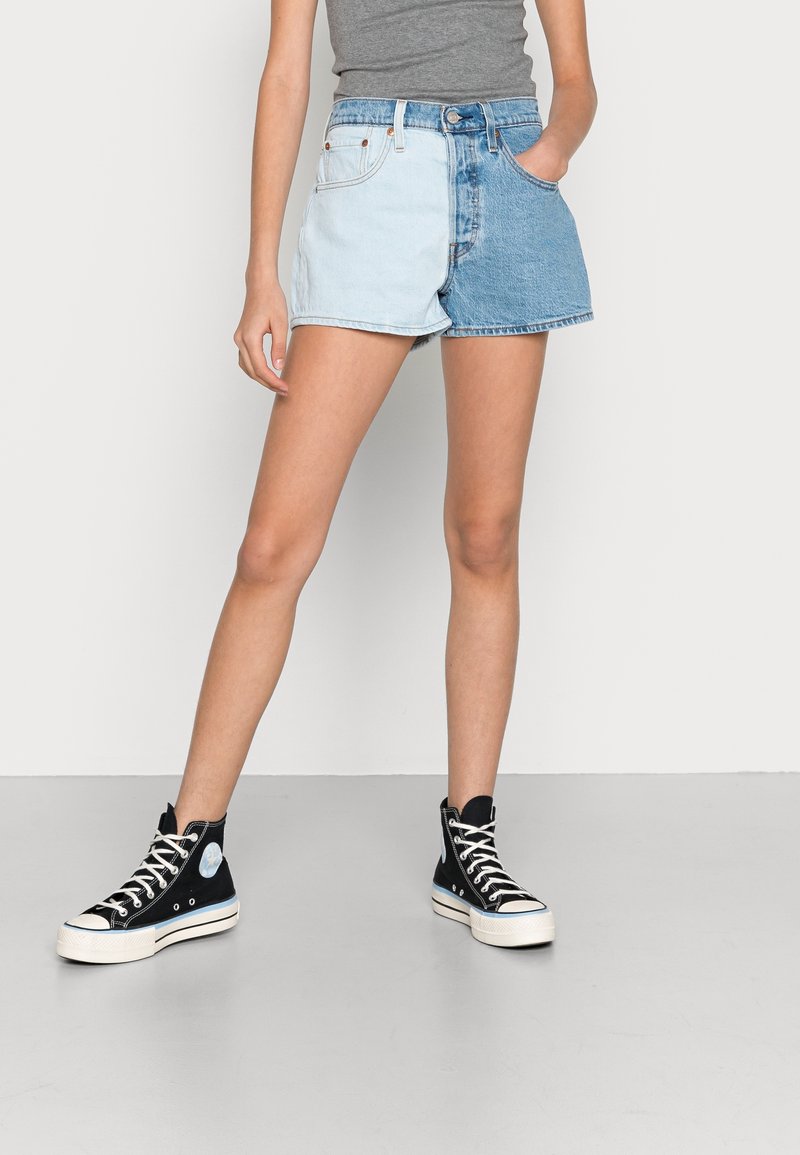 Shorts en denim avec un design en blocs de couleur présentant des sections bleues claires et foncées, associés à des baskets montantes noires avec des accents blancs.
