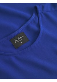 Top blu royal realizzato in tessuto liscio, con scollatura rotonda e etichetta nera con testo bianco che mostra marca e taglia.