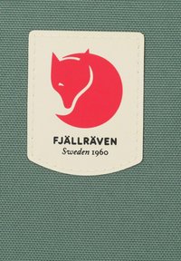 Fjällräven logotipo pleistras, kuriame pavaizduota raudona lapė ant apvalaus fono, rodomas ant tekstūruotos žalsvos medžiagos. Tekstas sako "FJÄLLRÄVEN Švedija 1960."