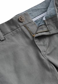 Pantaloni di tessuto grigio con una consistenza liscia, dotati di un bottone in rame, una zip in ottone e una fodera a righe blu in vita.